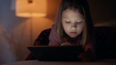 Sevimli küçük kız geceleri yatağında yatıyor, Tablet bilgisayar almıştır. Onun gece ışığı açık yanıyor. 