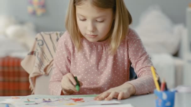 Roztomilá holčička v jejím pokoji u jejího stolu kreslí pastelkami. — Stock video