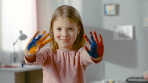 Χαριτωμένο και χαμογελαστό κορίτσι δείχνει τα χέρια καλύπτονται με πολύχρωμα χρώματα. — Αρχείο Βίντεο