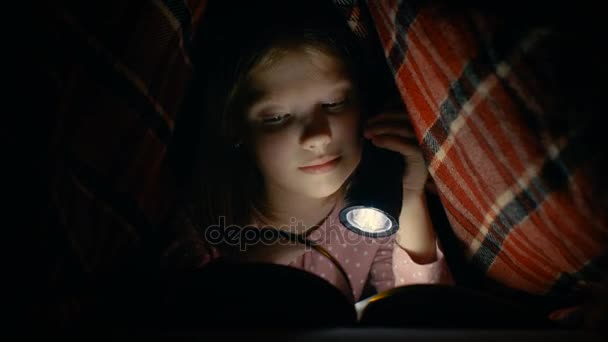 Smart Little Girl lit livre intéressant avec une lampe de poche sous la couverture . — Video