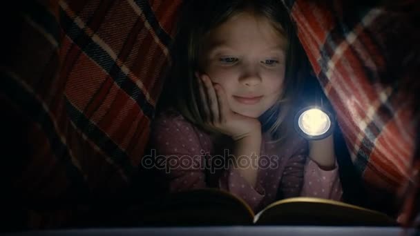 Inteligente niña lee interesante libro con una linterna debajo de la manta . — Vídeo de stock