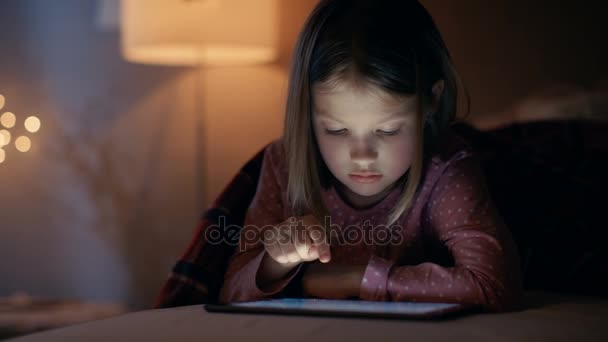 Мила дівчина лежить в її ліжку з портативного комп'ютера. Вона взаємодіє із пристроєм. Її кімнаті є затишний і ліжко вогні на. — стокове відео