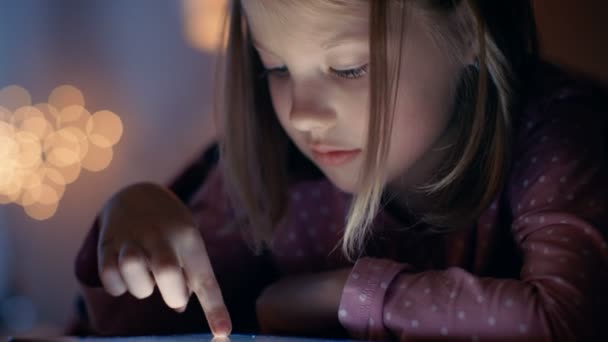Roztomilá mladá dívka leží v posteli s přenosným počítačem. Zařízení komunikuje. Její pokoj je útulná a postel světla jsou na. — Stock video