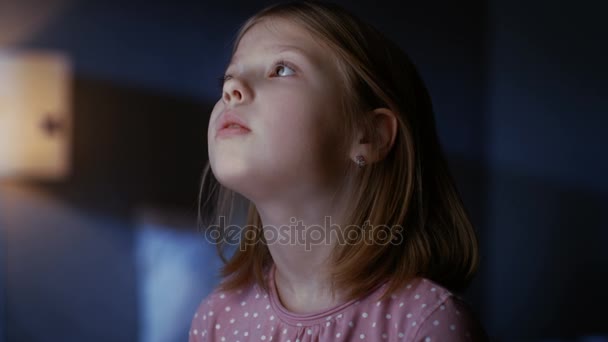 Curiosa niña en su dormitorio por la noche, se para de puntillas y mira por la ventana . — Vídeos de Stock