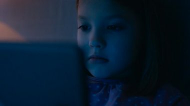 Sevimli genç kız Her yatakta yatıyor gece ve Tablet bilgisayar kullanır o aydınlatır yüz.
