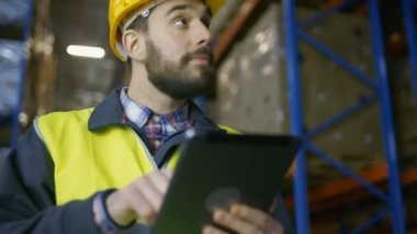 Arazi giyiyor zor şapka tutan Tablet bilgisayar ve sayar mal ambarındaki üzerlerine dolu kutular ile rafları.