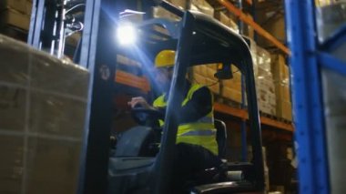 Yakın çekim Shot bir Forklift sürücüsü işletim aracın içinde büyük bir depo palet raf tam.