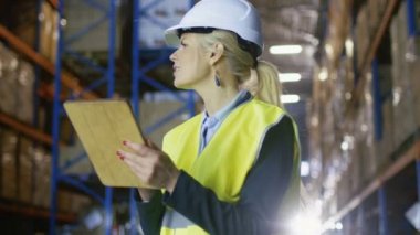 Kadın Surveyor kask giyiyor ve Holding Pano sayar mal duran büyük bir depo ile bu palet rafları.