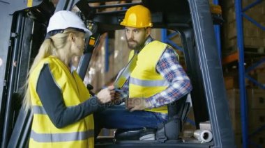 Kadın yönetici sürücü Forklift iş atama verir. Büyük bir depodalar palet raflar dolu.