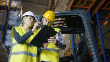 Pano yöneticisiyle erkek sürücü Forklift atama çalışma verir. Büyük bir depodalar palet raflar dolu.