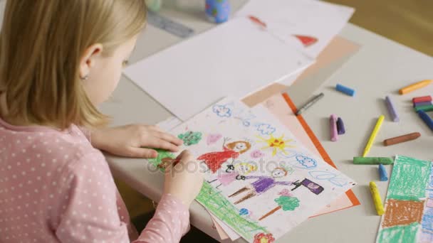 Sobre el hombro Vista de la linda niña dibujando su familia con lápices de colores . — Vídeos de Stock