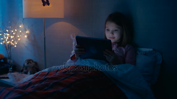 Menina bonito em seu quarto encontra-se na cama com tablet computador . — Vídeo de Stock