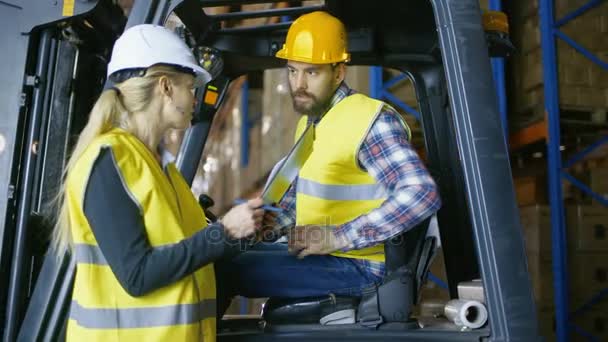 Kvinnliga handledare ger arbete tilldelning till gaffeltruck drivrutin. De är i en stor lagerlokal Full av pallställ. — Stockvideo