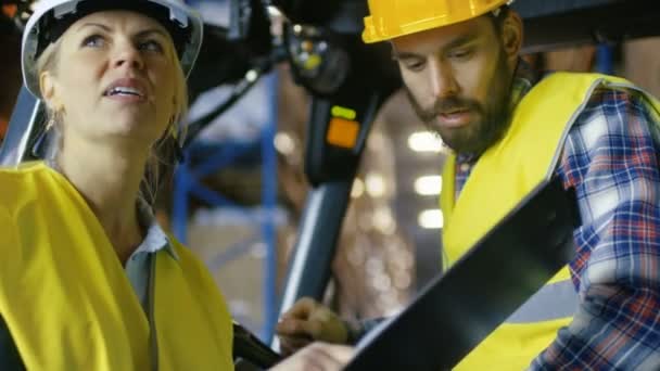 Gerente femenina con portapapeles da asignación de trabajo al conductor de la carretilla elevadora. Están en un gran almacén lleno de estantes de paletas . — Vídeo de stock