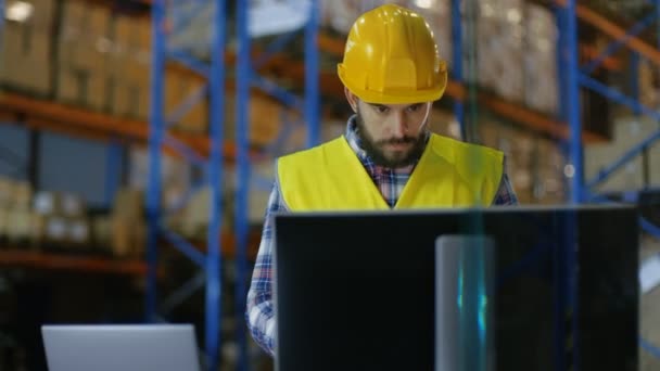 El inspector masculino que usa casco duro escribe en portapapeles y consulta su computadora personal. Está en el Gran Almacén con Filas de Paletas . — Vídeos de Stock