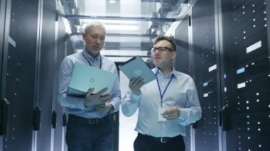 İki, bu veri merkezinde sunucu rafları satırları arasında yürüyüş mühendisler. Tablet bilgisayar ve Laptop üzerinde çalışmak.