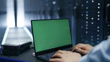 Bu teknisyen üzerinde çalışıyor yeşil ekran Chroma anahtar ile bir dizüstü bilgisayar büyük veri merkezindeki sunucu rafları satır içinde.