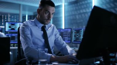 Oda izleme içinde birden çok ekranı ile kendi bilgisayarında çalışan teknik mühendis close-up. Onun meslektaşları ile grafik ve onların monitörlerde çeşitli verileri arka planda.