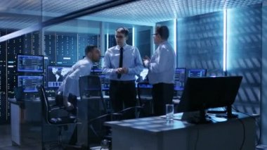 Teknik moderatörlerin ekip Oda izleme etkin tartışma var. Sistem kontrol odası çalışma görüntüler gösteren çeşitli veri ve sahip sunucular raflar dolu.