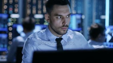 Ondan önce birden çok ekranı ile onun masasında oturan bir profesyonel teknik denetleyicisi close-up. Arka planda izleme çalışma arkadaşları Oda.