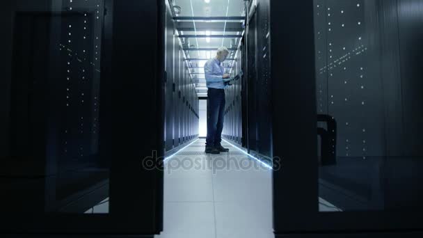 La porte du centre de données s'ouvre et nous voyons l'ingénieur serveur travailler sur un ordinateur portable. Cabinet de serveur de rack est ouvert .