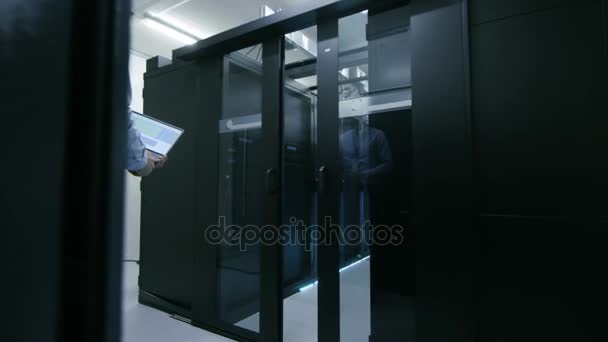 Im Rechenzentrum betritt der Ingenieur mit dem Notizbuch Schiebetüren. von seinen Seiten arbeitende Server-Racks. — Stockvideo
