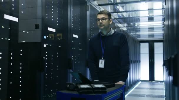 Técnico de TI en centro de datos empuja carro de choque a través de puertas correderas. Filas de servidores de rack de trabajo son visibles . — Vídeo de stock