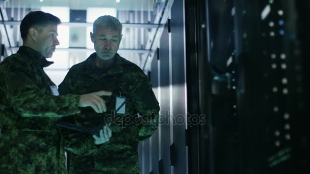 En el centro de datos, dos militares trabajan con el gabinete de bastidor de servidor abierto. Uno sostiene la edición militar del ordenador portátil . — Vídeos de Stock