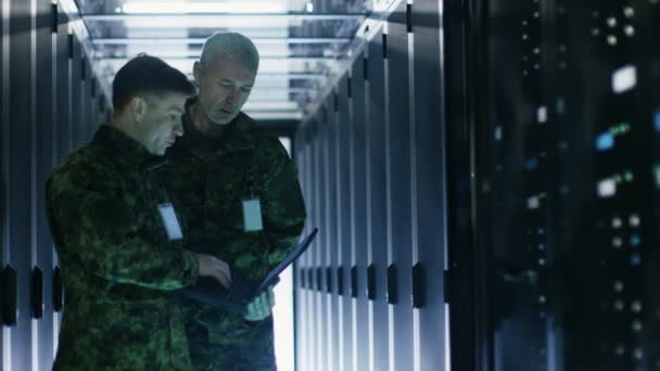 En el centro de datos, dos militares trabajan con el gabinete de bastidor de servidor abierto. Uno sostiene la edición militar del ordenador portátil . — Vídeos de Stock
