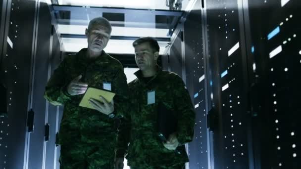 Due soldati che camminano nel corridoio del data center. Uno tiene il computer Tablet, Hanno discussione. Righe di server di dati di lavoro dai loro lati . — Video Stock