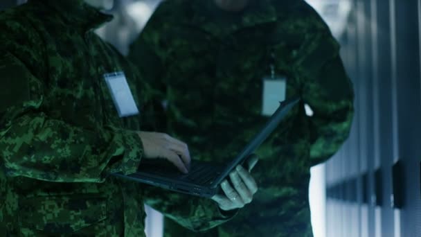 En el centro de datos, dos militares trabajan con el gabinete de bastidor de servidor abierto. Uno sostiene la edición militar del ordenador portátil . — Vídeo de stock