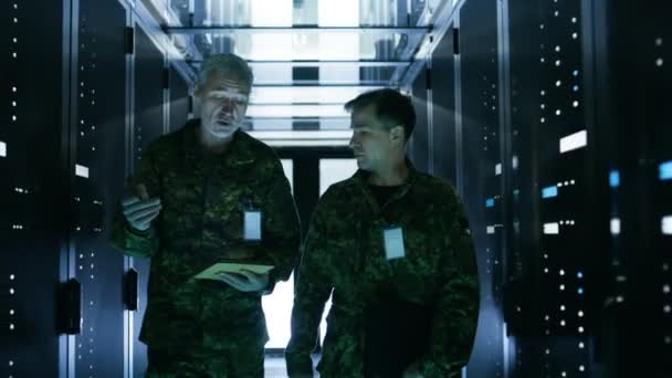 Zwei Soldaten auf dem Weg in den Korridor des Rechenzentrums. Man hält Tablet-Computer in der Hand, man diskutiert. Reihen funktionierender Datenserver an ihren Seiten. — Stockvideo