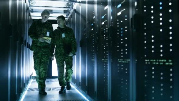 Två militära män som gick i datacenter korridor. Använder en Tablet PC, de har diskussion. Rader av arbetar dataservrar sidorna. — Stockvideo