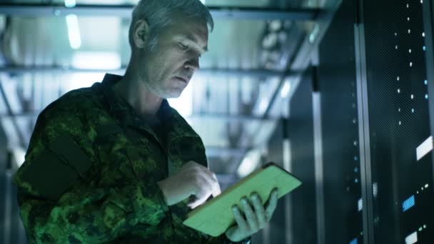 Στρατιωτικός άνδρας στο κέντρο δεδομένων χρησιμοποιεί υπολογιστή Tablet. Σειρές από ράφια Server έχουν δει. — Αρχείο Βίντεο