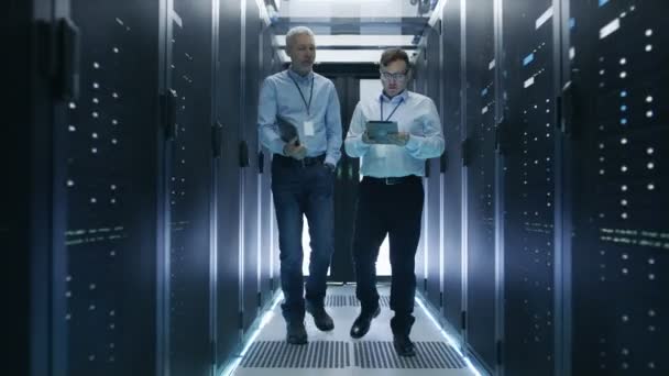 Twee Server technicus werken in datacenter. Gebruik van een Tablet PC. Ze lopen door rijen van Server Racks. — Stockvideo