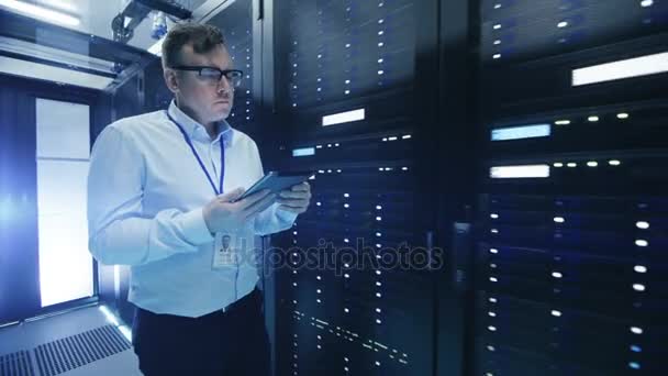 Після зйомок ІТ-інженера, що йде через центр обробки даних коридор з рядами серверів стійки. Він використовує планшетний комп'ютер . — стокове відео