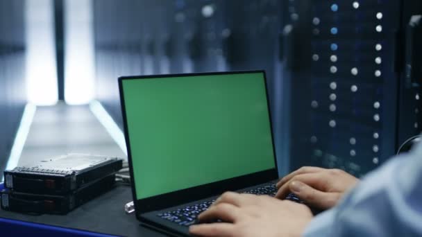 O técnico de TI está trabalhando em um laptop chave Chroma de tela verde no Big Data Center com linhas de rack de servidor nele . — Vídeo de Stock