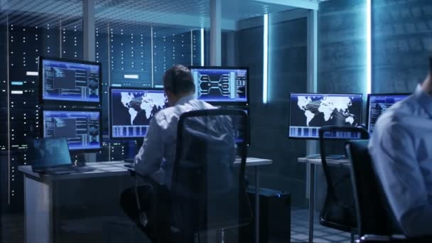 Zwei IT-Profis, die in einem Überwachungsraum mit mehreren Displays arbeiten, die sie umgeben.System-Leitwarte hat es auf Serverschränken. — Stockvideo