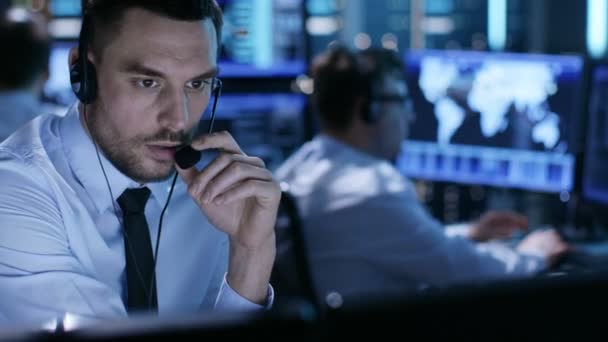 Dans la salle de surveillance, le spécialiste du soutien technique parle dans le casque. Ses collègues travaillent en arrière-plan 