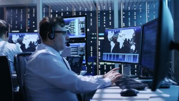 Kameran flyger aktivt genom System Control Center visar professionella säkerhetspersonal som arbetar på sina arbetsstationer med flera bildskärmar. — Stockvideo
