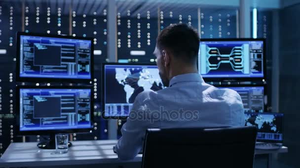 Τεχνικός ελεγκτής λειτουργεί στη θέση εργασίας του με πολλαπλές οθόνες. Οθόνες δείχνουν διάφορες τεχνικές πληροφορίες. Είναι μόνος στο κέντρο ελέγχου του συστήματος. — Αρχείο Βίντεο