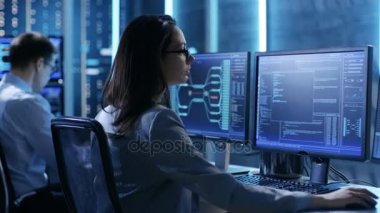 Kadın mühendis denetleyicisi çalışma sisteminin gözlemler. Arka plan kişilerde çalışma ve monitörler çeşitli bilgileri göster. 