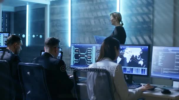В Центре управления государственной системой. Женщина-супервайзер с ноутбуком проводит встречу для своей команды инженеров. Номер оснащен несколькими дисплеями с различной информацией . — стоковое видео