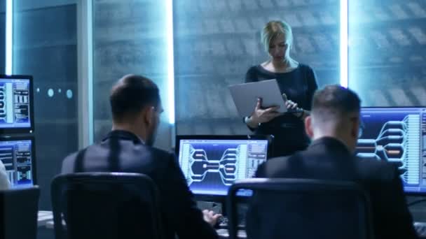 I Regeringens System Control Center. Kvindelig Supervisor med Laptop Holds møde for hendes team af ingeniører. Værelset er udstyret med flere skærme, der viser forskellige oplysninger . – Stock-video