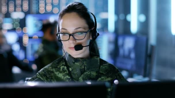 Kvindelig militær teknisk support Professionel giver instruktioner i headset. Hun er i et overvågningsrum med andre officerer og mange arbejdsskærme. . – Stock-video