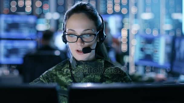 Femme militaire soutien technique professionnel donne des instructions dans casque. Elle est dans une salle de surveillance avec d'autres officiers et de nombreux écrans de travail . — Video