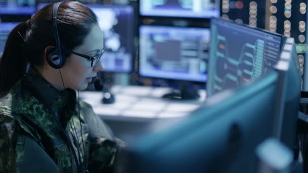 Mujer Militar Soporte Técnico Profesional Da instrucciones en los auriculares. Está en una sala de monitoreo con muchas pantallas de trabajo . — Vídeo de stock