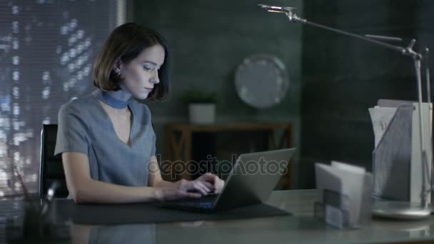 Стильный топ-менеджер работает над ноутбуком в своем личном офисе с видом на большой город. Ее рабочее место сделано в темных тонах, с обнаженными цементными стенами . — стоковое видео