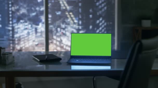 Närbild bilder av en bärbar dator med gröna Mock-up skärmen står på ett träbord. I vyn bakgrund storstad fönster. — Stockvideo