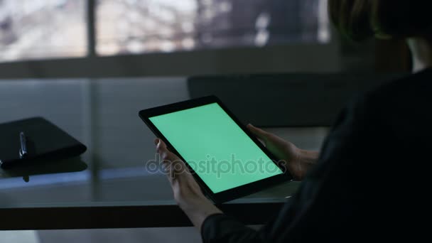 Přes rameno pohled podnikatelka sedí u stolu a tabletový počítač pomocí zeleným plátnem. Velké město je vidět z okna. — Stock video